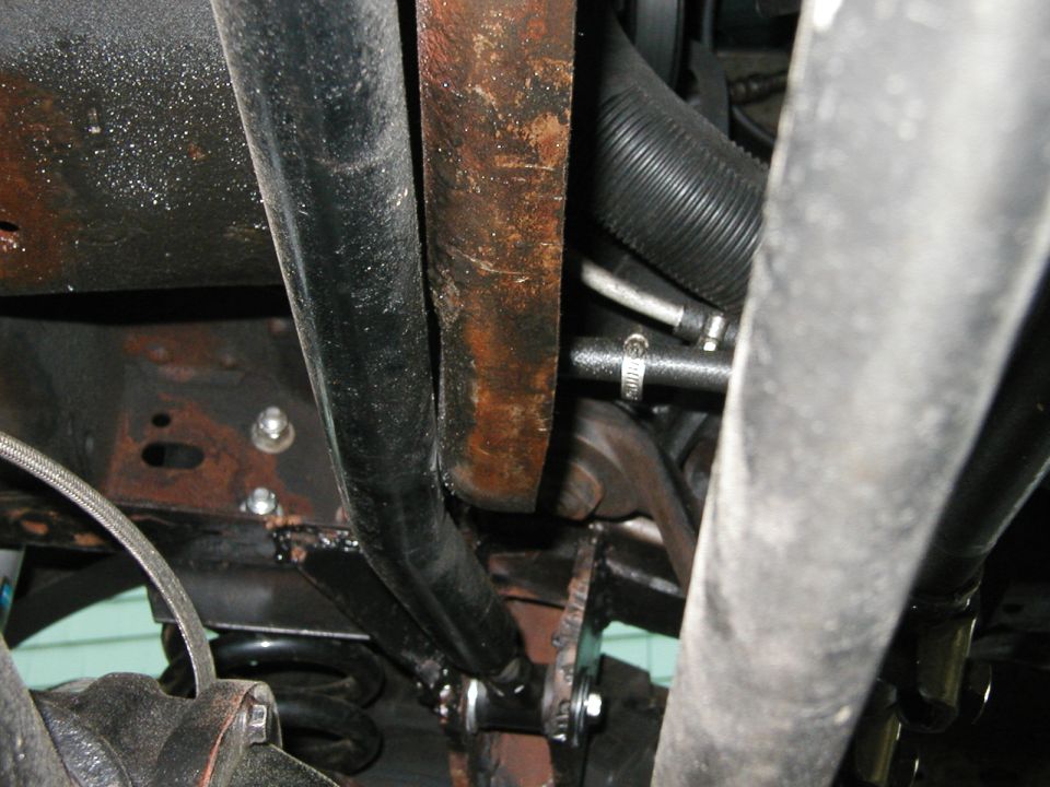 Undercarriage view showing suspension, exhaust pipes, and hoses. Some rust is visible on metal components