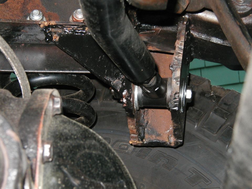 Close-up of rusty metal brackets and a black bar attached to a coil spring and tire