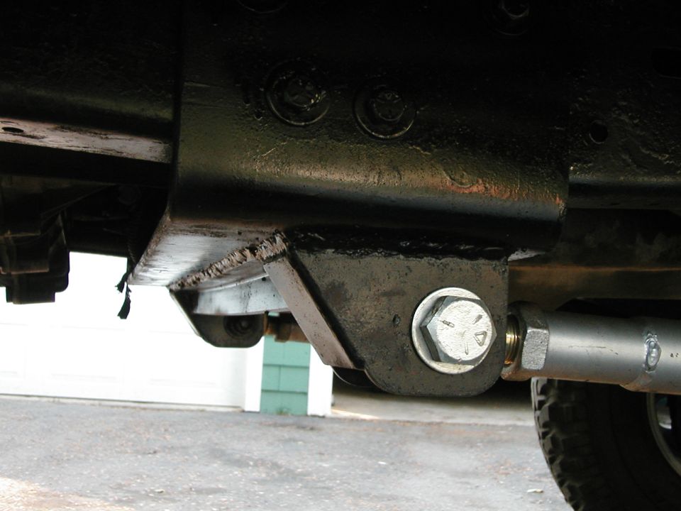 Close-up of a vehicle's undercarriage showing a metal bracket bolted to the frame with a suspension component attached