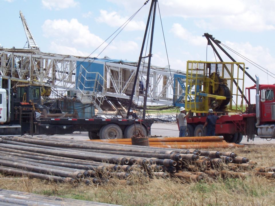 Red oilfield winch truck and flatbed trailer with a lowered drilling mast and stacked drill pipe