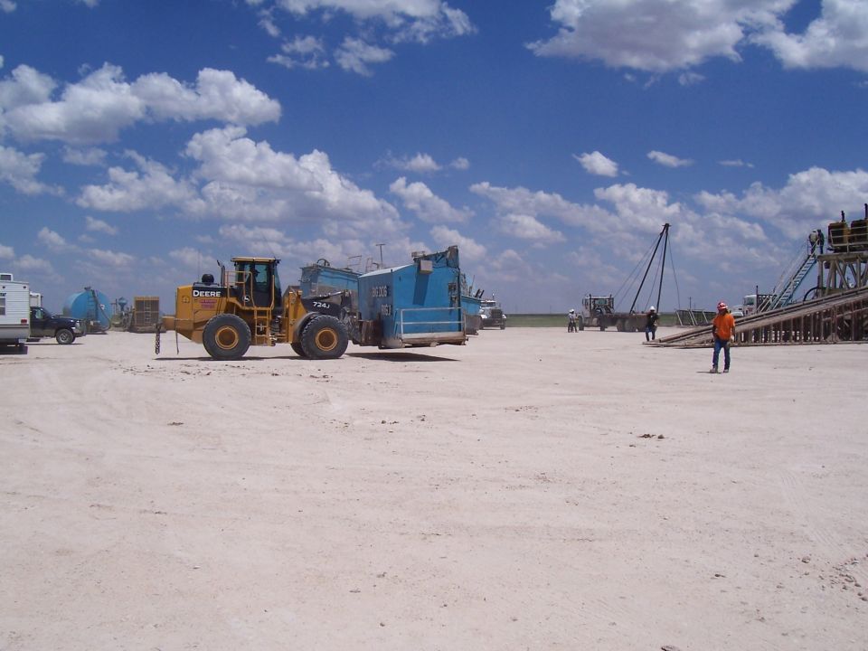 yellow John Deere loader and blue industrial equipment at a construction site under a cloudy sky
