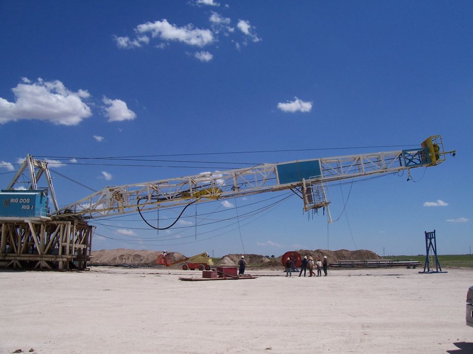 Oil rig labeled 'BIG DOG RIG 1' under a blue sky with clouds. Workers are visible near the base of the rig