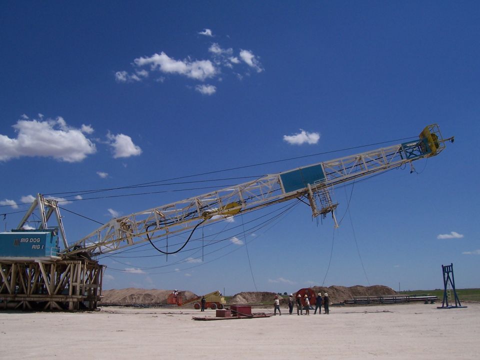 Drilling rig with "BIG DOG RIG 1" text, extended boom against blue sky with clouds