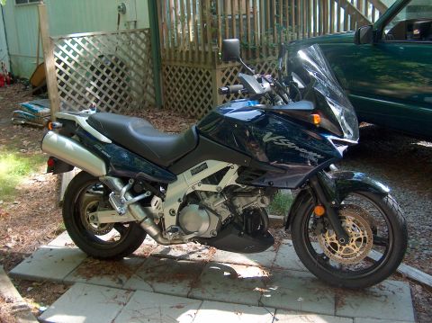 2002 Suzuki TL1000R - A Suzuki V-Strom motorcycle is parked on paving stones next to a wooden fence and a green SUV.