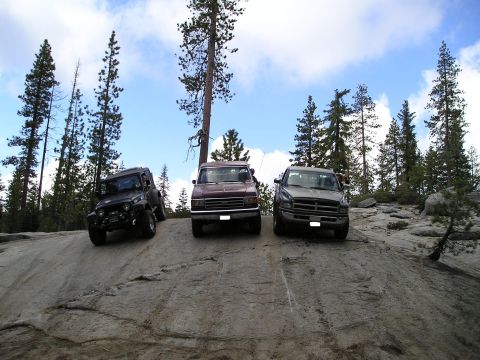 1989 Ford Bronco - A Jeep, a maroon van, and a gray truck are parked on a rocky slope in a forest setting.