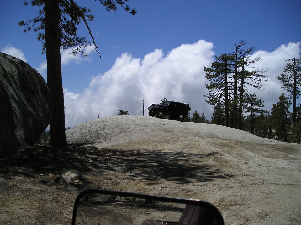 Black SUV parked on a large rock formation with trees and clouds in the background