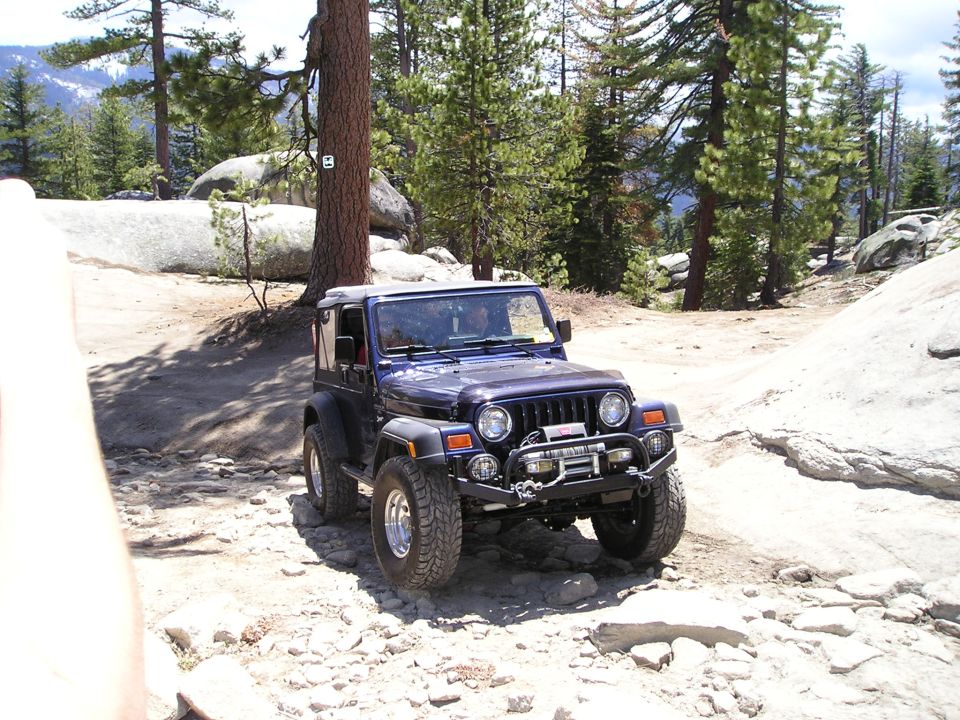 Dark blue Jeep Wrangler TJ parked on a rocky, wooded trail