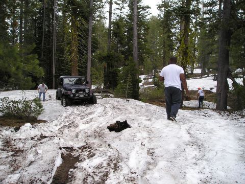1989 Ford Bronco - A Jeep Wrangler navigates a snow-covered mountain path with two people observing.