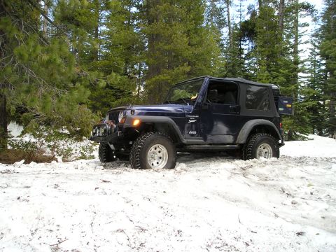 1989 Ford Bronco - A dark blue Jeep Wrangler navigates through a snowy forest trail.