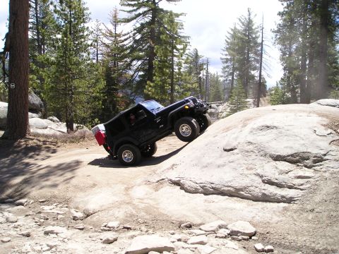 1989 Ford Bronco - A black Jeep Wrangler navigates a rocky off-road trail in a wooded mountain area.