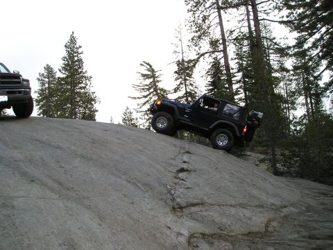1989 Ford Bronco - Two off-road vehicles navigate a rocky incline in a wooded area.