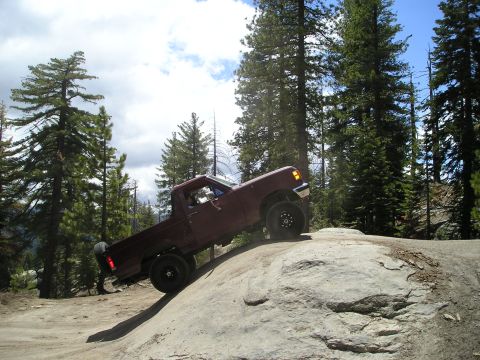 1989 Ford Bronco - A red pickup truck navigates a rocky trail in a wooded mountain area.