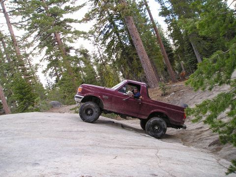1989 Ford Bronco - 1989 Ford Bronco navigating a steep, rocky trail in a wooded mountain area.