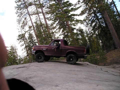 1989 Ford Bronco - A maroon Ford Bronco navigates a rocky incline in a forested mountain area.