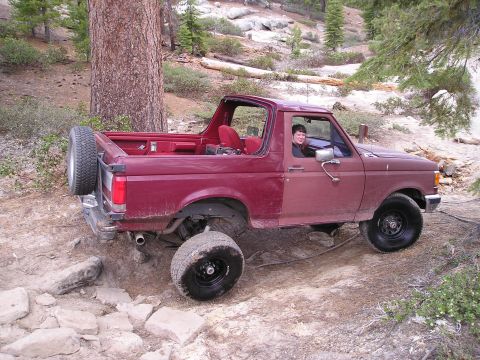 1989 Ford Bronco - This SUV is navigating a challenging, rocky terrain in a wooded area.