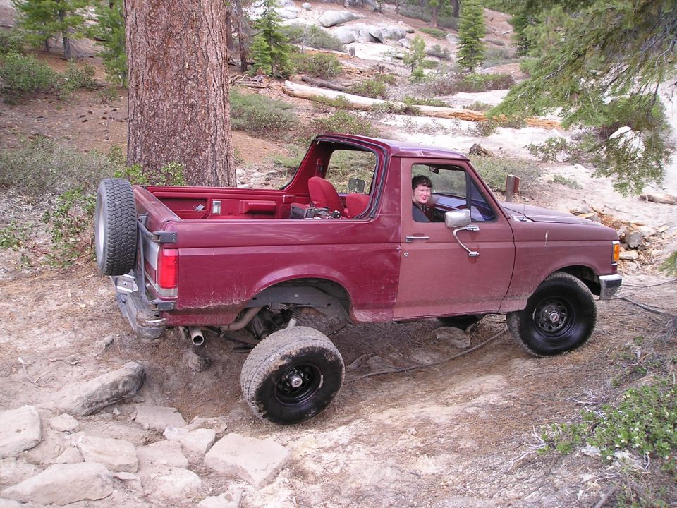 Maroon SUV with spare tire on back driving on rocky trail, person in driver's seat