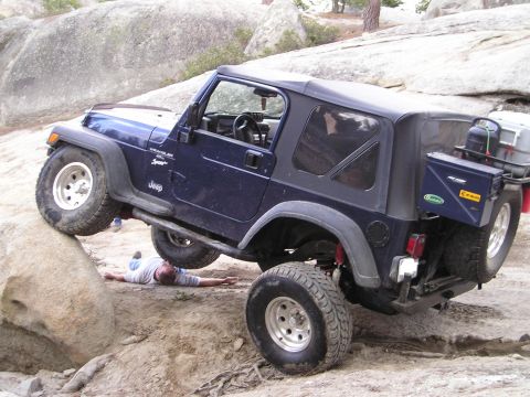 1989 Ford Bronco - Jeep Wrangler TJ navigating rocky terrain with a person lying beneath it.