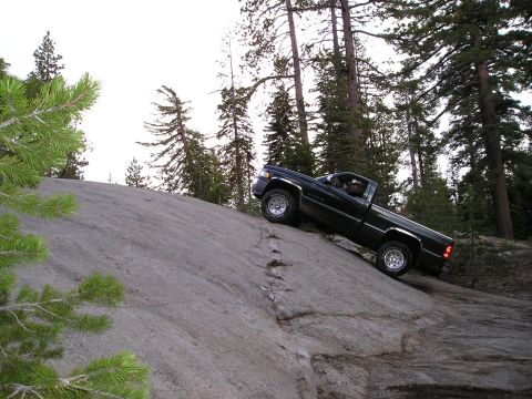 1989 Ford Bronco - Pickup truck navigating a steep rock incline in a wooded mountain area.