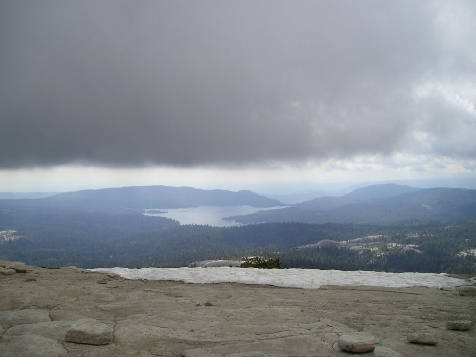 Mountain range with a lake under a cloudy sky. Snow patches on the rocky foreground