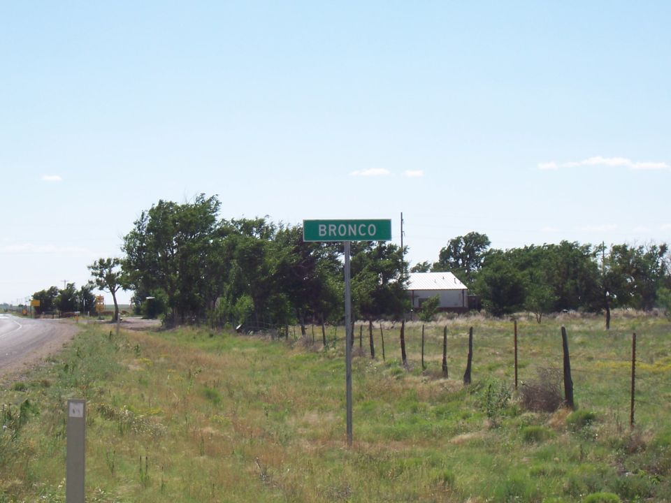 Green roadside sign reading BRONCO with a white building and trees in the background