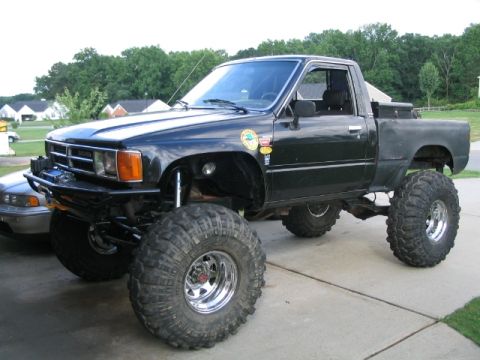 1986 Ford F-150 - Modified Toyota pickup truck with significant lift and oversized tires parked on a driveway.