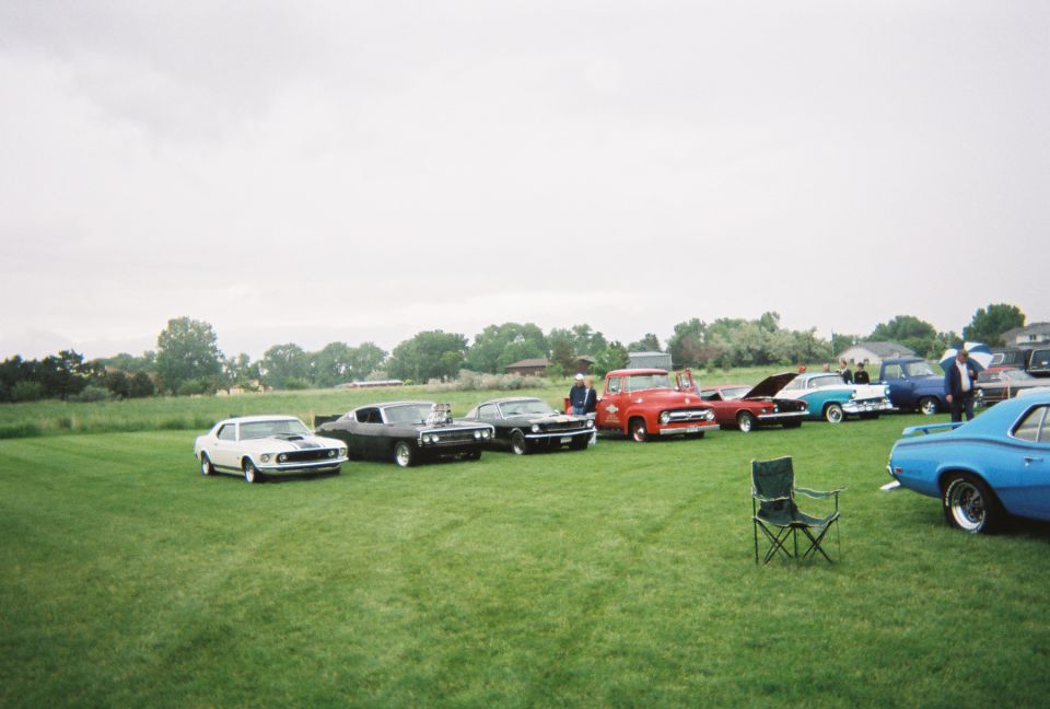 Row of classic muscle cars and a red 1950s pickup lined up on grass at a car show