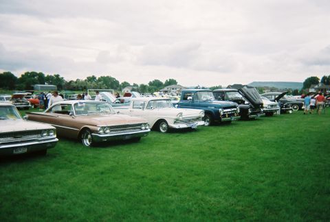 1972 Ford Ranchero - A row of vintage Ford vehicles, including a 1959 Fairlane, are displayed on a grassy field under a cloudy sky.