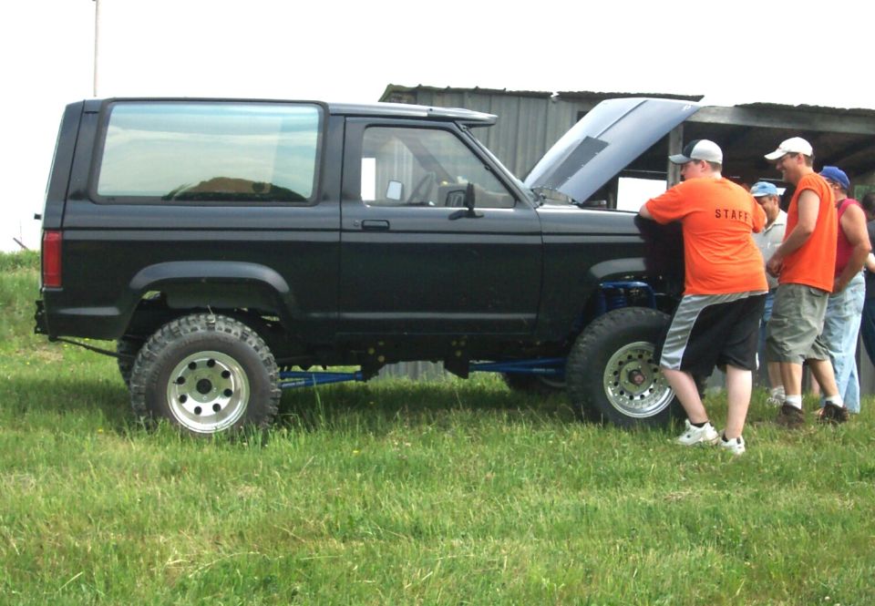 Black lifted Bronco II with open hood surrounded by a small crowd at an event