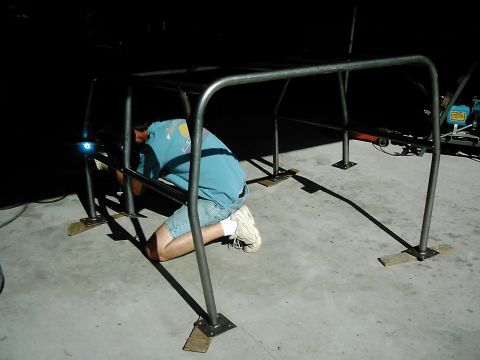 1978 Ford Bronco - A person is welding a custom roll cage structure on a concrete floor.
