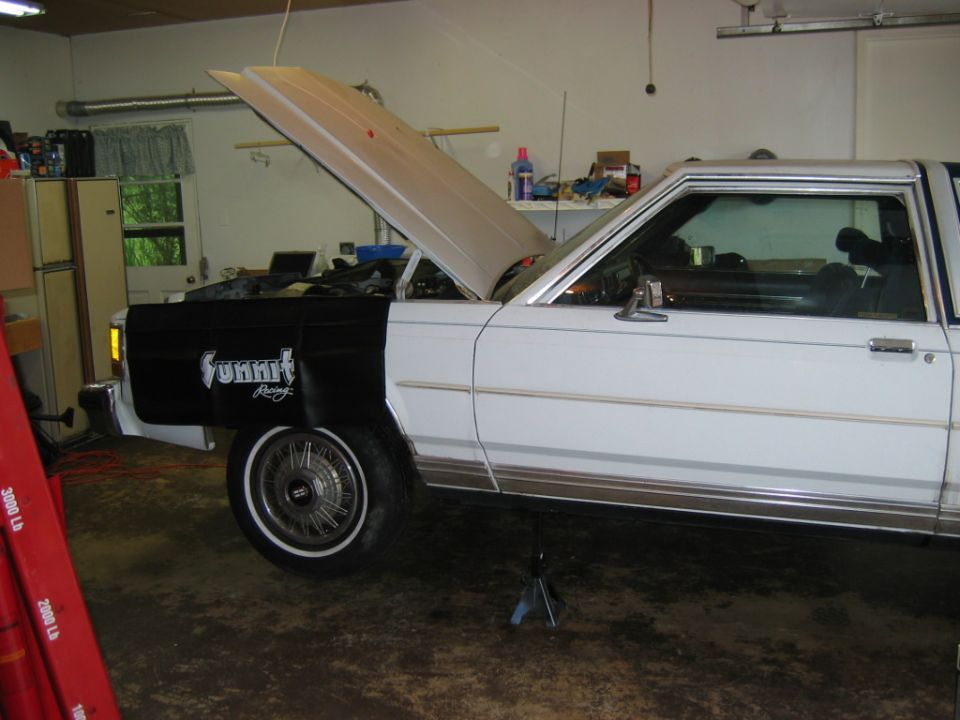 White Ford Crown Victoria with hood open, black fender cover with "Summit Racing" text