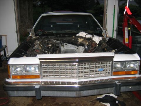 1985 Ford Crown Victoria LTD - Front view of a 1985 Ford Crown Victoria LTD with its engine removed, undergoing work in a garage.