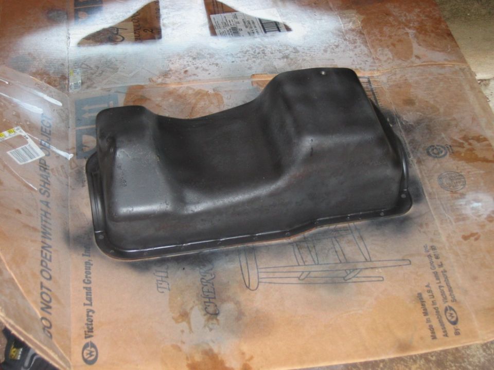 Black oil pan sitting on cardboard with spray paint overspray