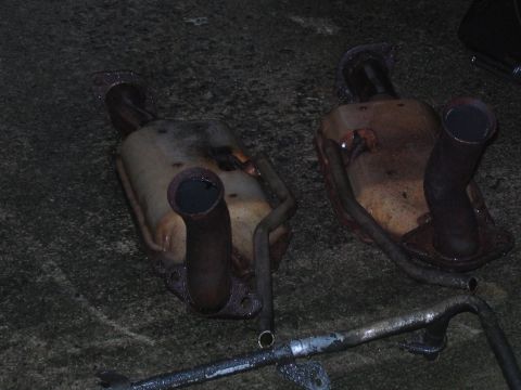 1985 Ford Crown Victoria LTD - Two old exhaust mufflers and exhaust pipes are lying on a dark, textured surface.