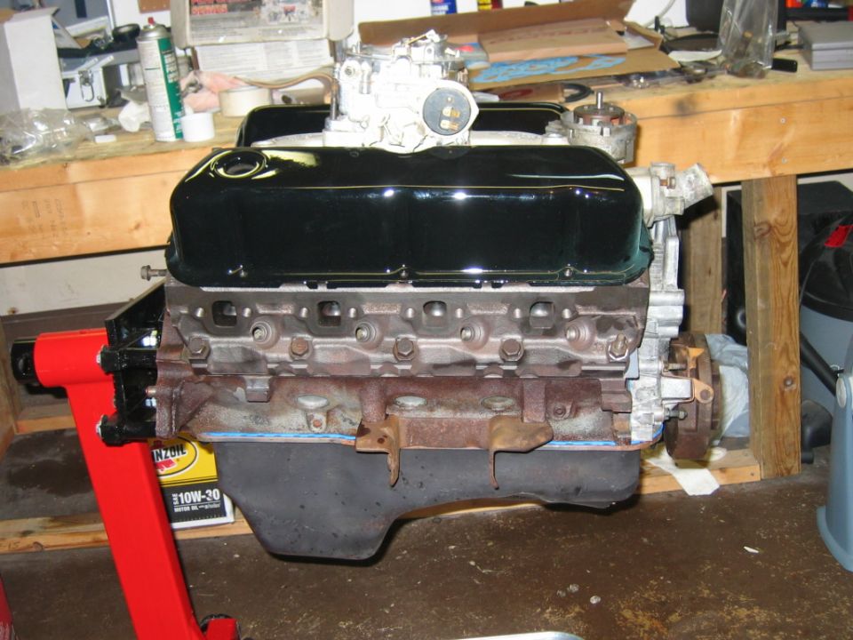 V8 engine on a red stand, with black valve covers and a carburetor