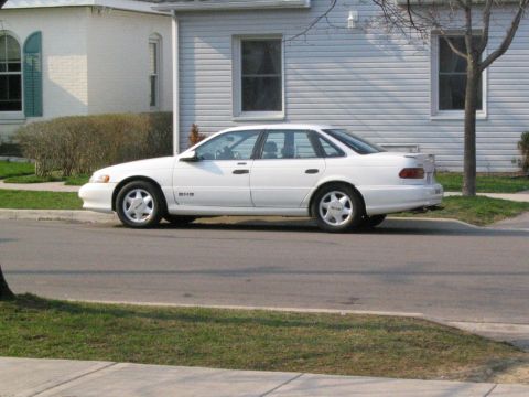 1993 Ford Taurus - A white 1993 Ford Taurus is parked on the street in front of a house.