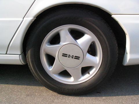 1993 Ford Taurus - A close-up view of a silver wheel on a white vehicle, showing the SHS logo.