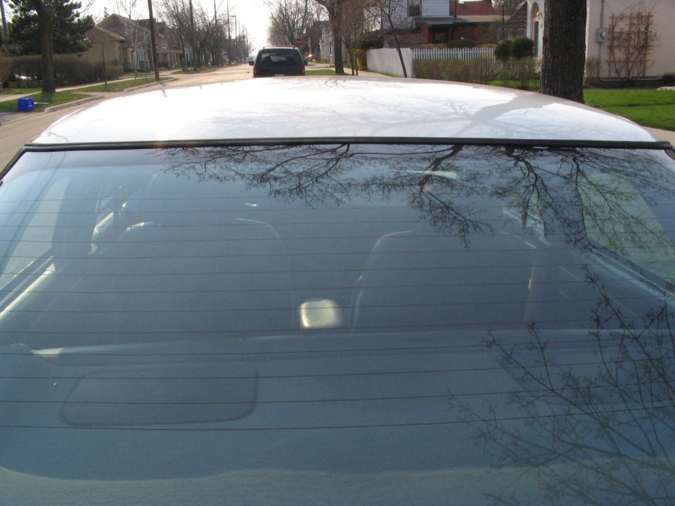 Rear window and roofline of a car, with another car visible in the distance on a residential street
