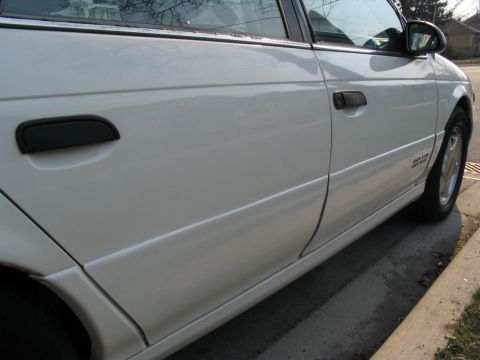 1993 Ford Taurus - The side profile of a white sedan is captured, showing its doors and a portion of the rear wheel.