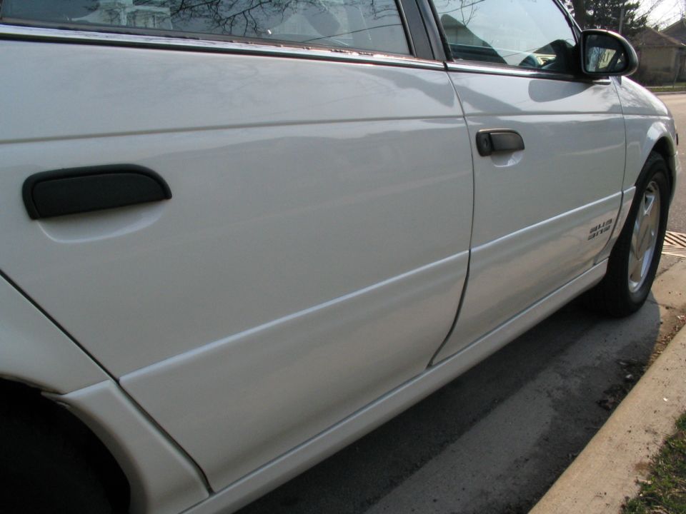 Low side view of white sedan's doors, rocker cladding and silver five-spoke wheel