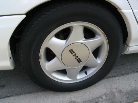 1993 Ford Taurus - A close-up of a car's wheel shows a silver rim with a black tire and a distinctive center cap logo.
