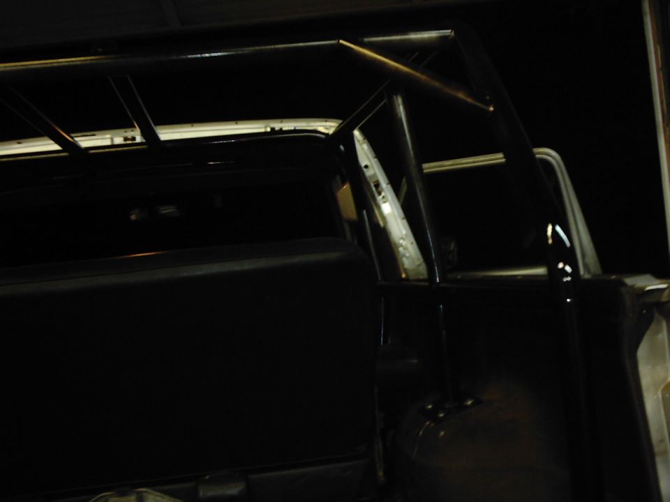 Roll cage installed inside a vehicle. The cage covers the rear passenger area and extends to the roof