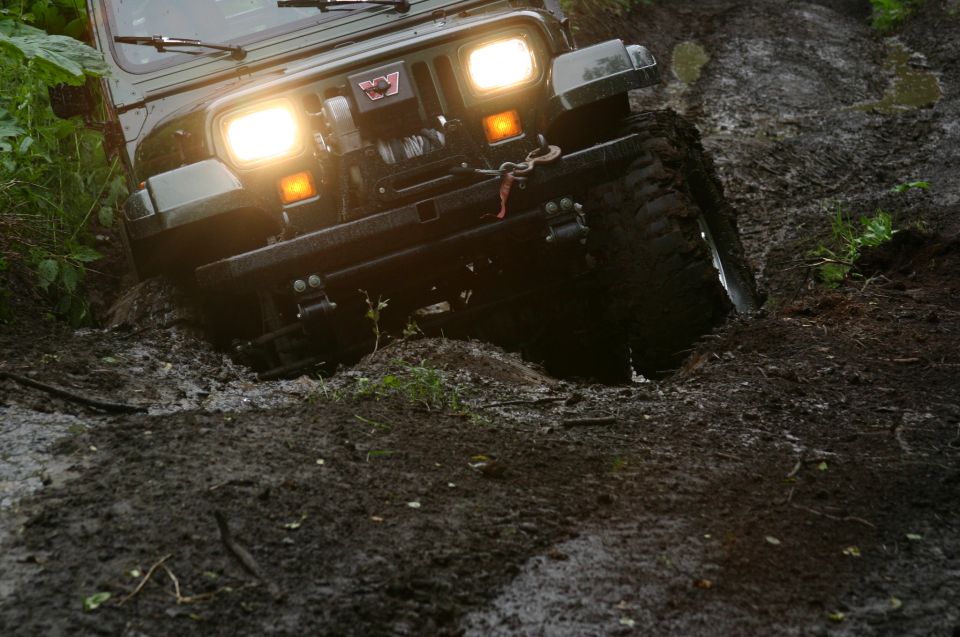 Winch-equipped 4x4 with headlights on dropping into a deep mud rut on a trail