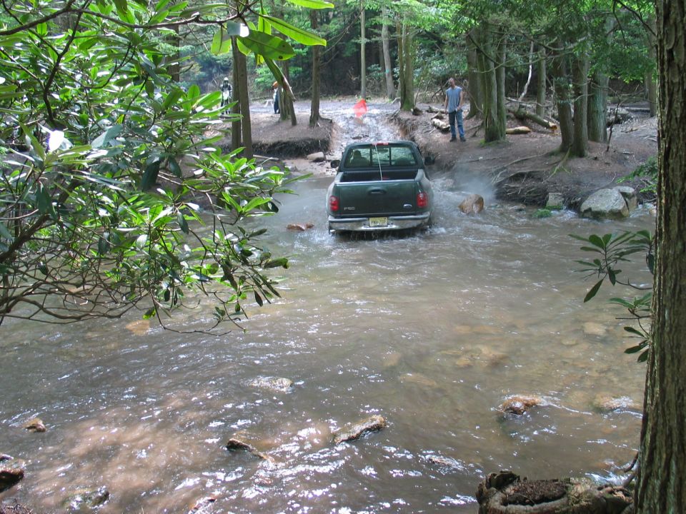 Dark green Ford F-150 pickup crossing a rocky creek on a wooded off-road trail