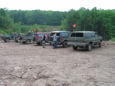 1995 Ford Bronco - Several SUVs and trucks are parked in a line on a dirt lot, with trees in the background.