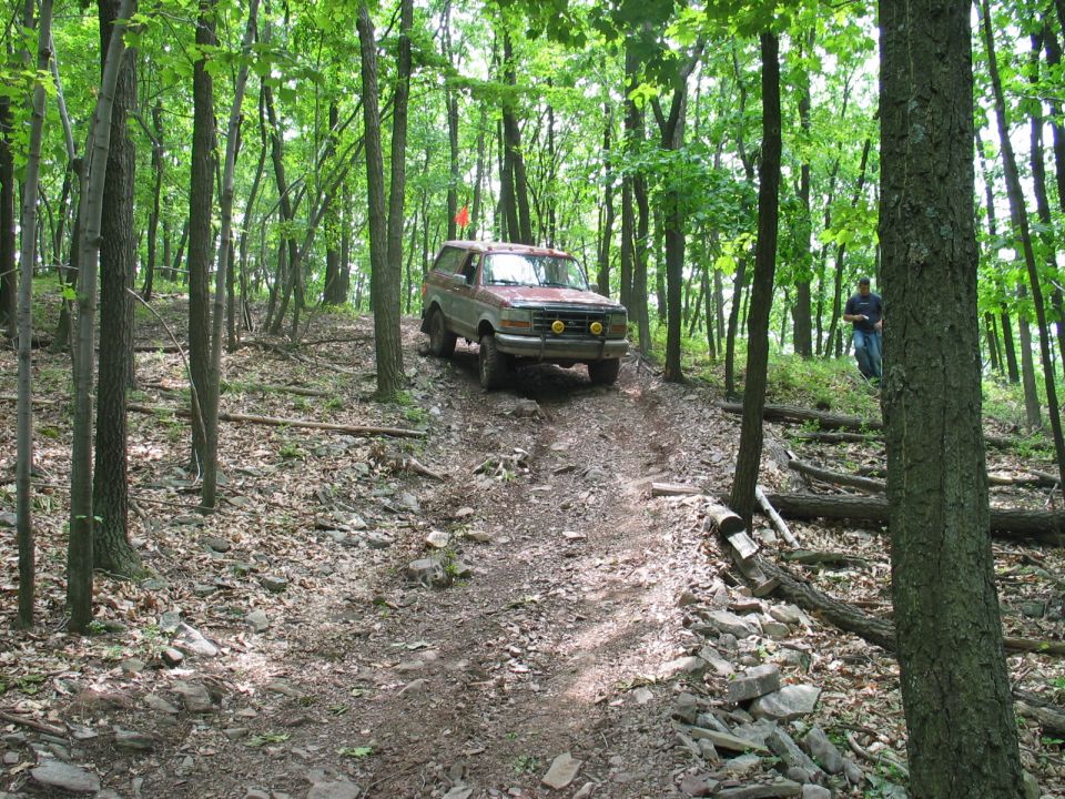 Red Ford SUV with brush guard cresting a rocky wooded off-road trail
