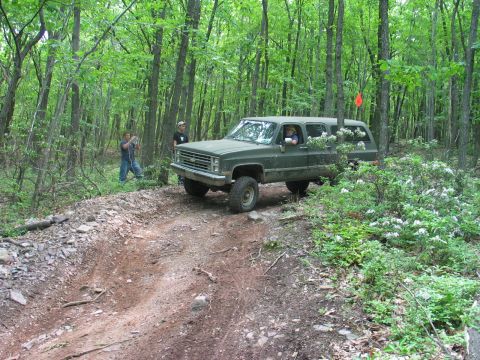 1995 Ford Bronco - A green SUV navigates a wooded trail, with two onlookers observing its progress.