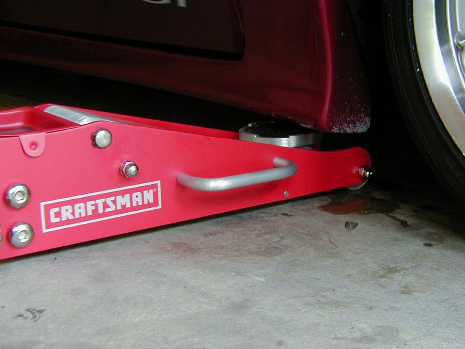 Red Craftsman car jack lifting the side of a red vehicle near a tire