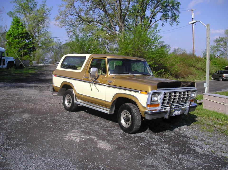 Gold and cream 1979 Ford Bronco parked on gravel, front three-quarter view with chrome grille and hood deflector