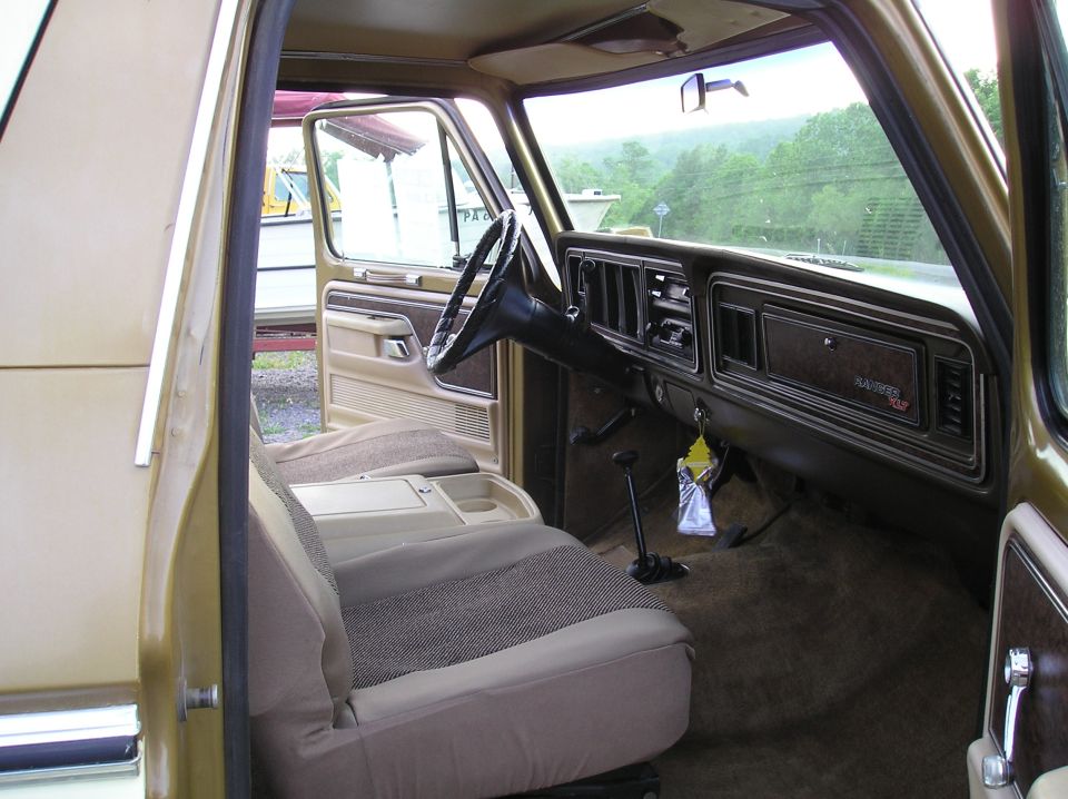 Tan and brown interior of a gold Ford with Ranger XLT dash badge, bench seat and floor shifter, seen through open passenger door