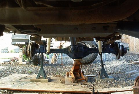 1986 Ford Bronco - The rear axle assembly of a vehicle is supported by jack stands and a floor jack for maintenance.